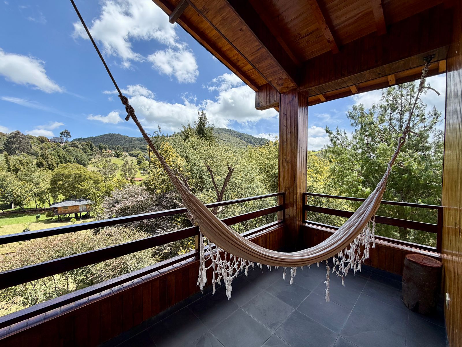 Balcón de madera con hamaca y vista a los bosques y montañas de Guasca